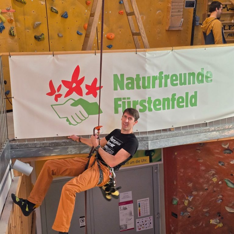 Banner der Naturfreunde Fürstenfeld vor einer Kletterwand, Veranstaltung mit Zuschauern.