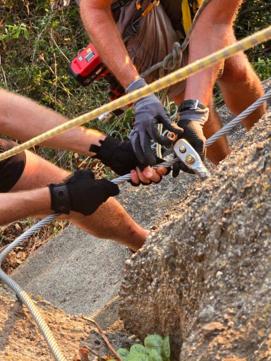 Hände von Kletterern, die eine Sicherung an einem Felsen anbringen.