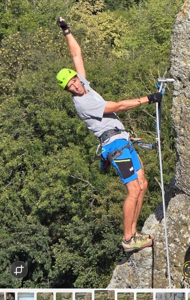Ein Kletterer in sportlicher Ausrüstung greift nach oben an einer Felswand.