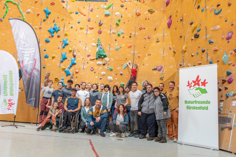 Gruppenfoto vor einer Kletterwand mit bunten Griffen und einem Banner.