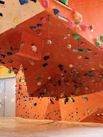 Boulderwand mit grellen Griffen und verschiedenen Kletterbereichen in einem Innenraum.