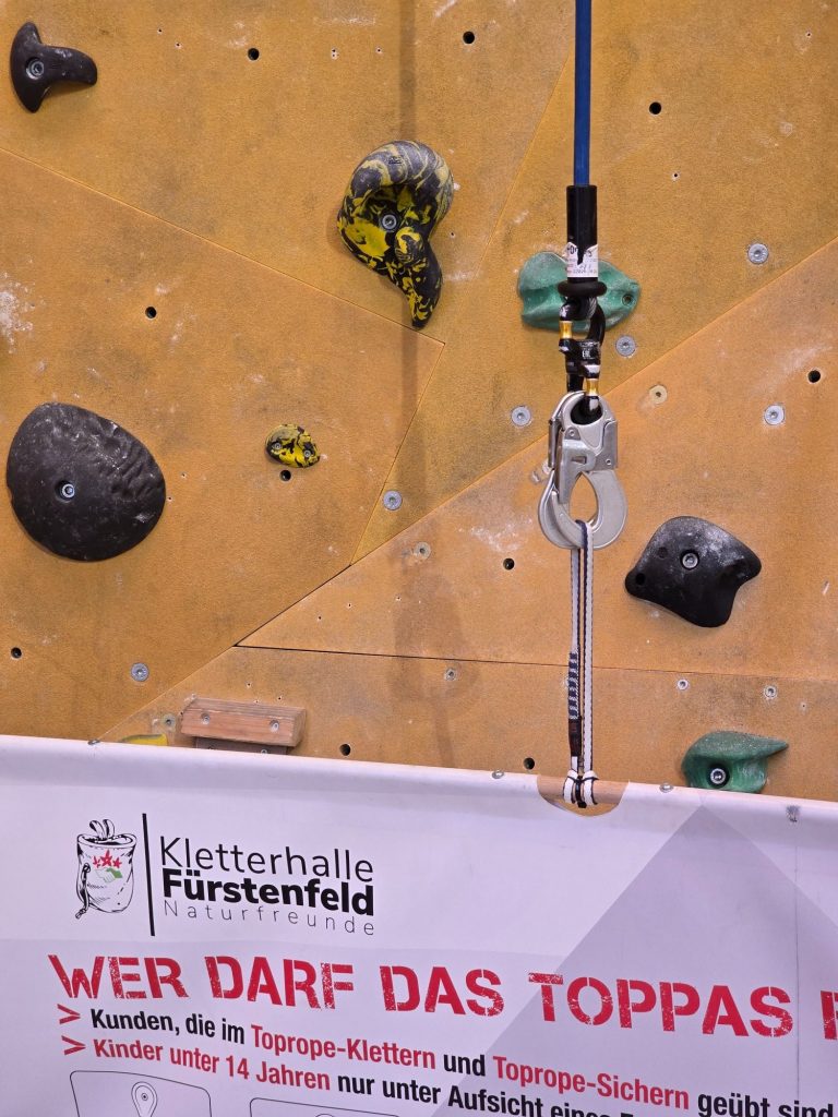 Greifpunkt einer Kletterwand mit Sicherungsgerät und einer bunten Klettergriffe.