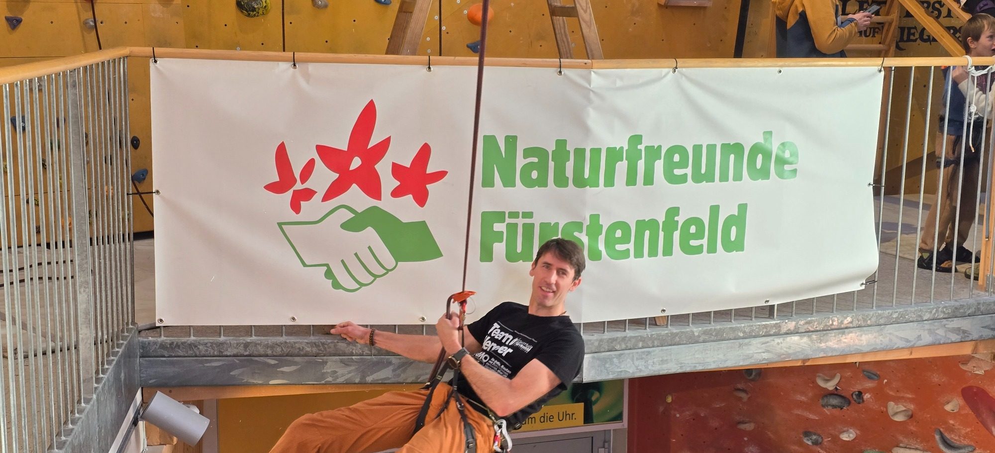 Nachwuchs Kletterer der Kletterhalle Fürstenfeld Gruppe von Kindern und Erwachsenen in Kletterausrüstung, lächelnd vor einer Kletterwand.