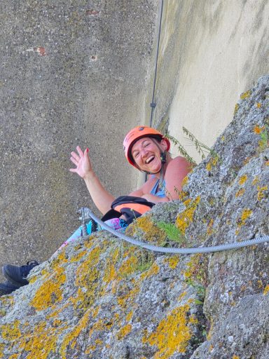 Lächelnde Person in Kletterausrüstung, die an einer Felswand hängt.