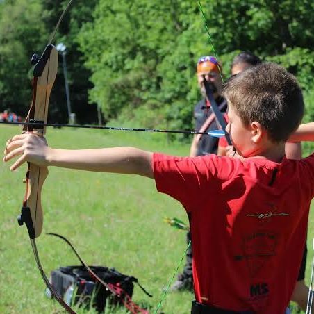 Ein Junge spannt einen Bogen auf einer Wiese während eines Bogenschießen-Events.