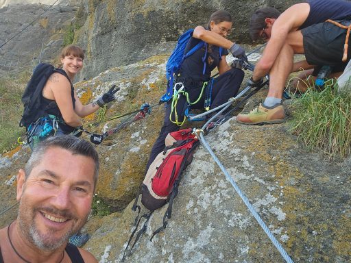 Vier Personen beim Klettern an Felsen, lächeln und sichern sich gegenseitig.