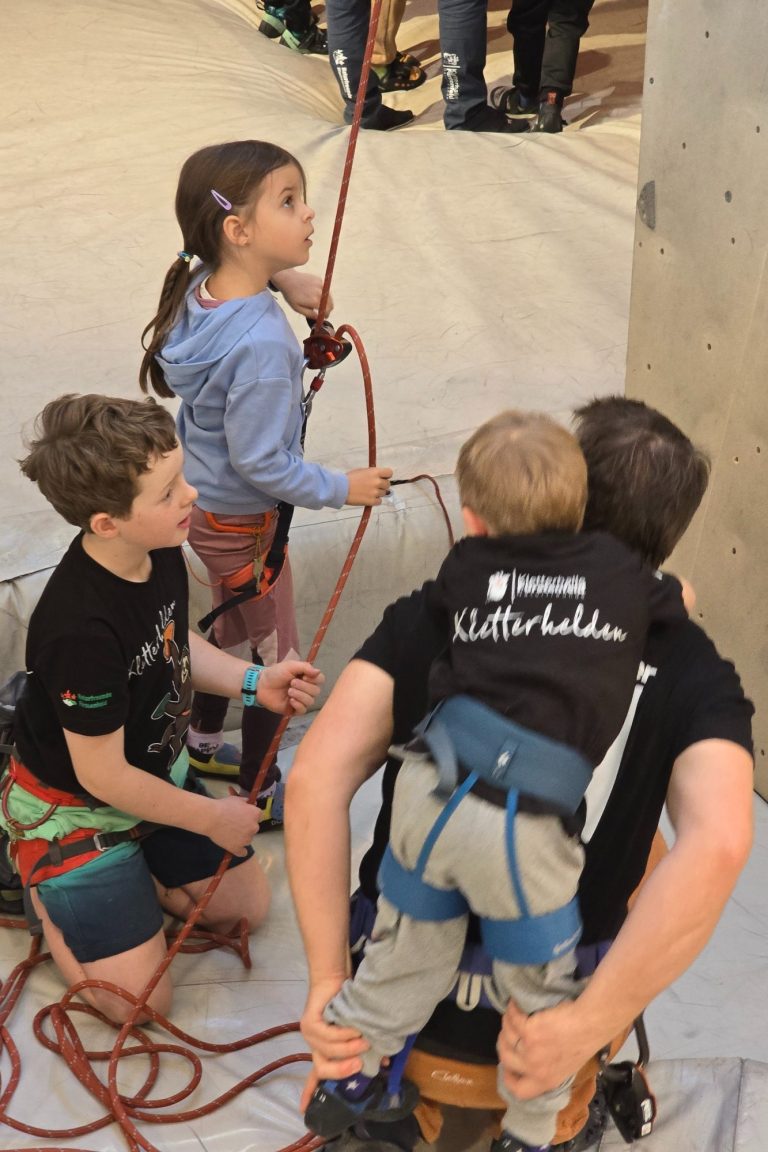 Drei Kinder beim Klettern, eines wird unterstützt, während ein anderes zuschaut.