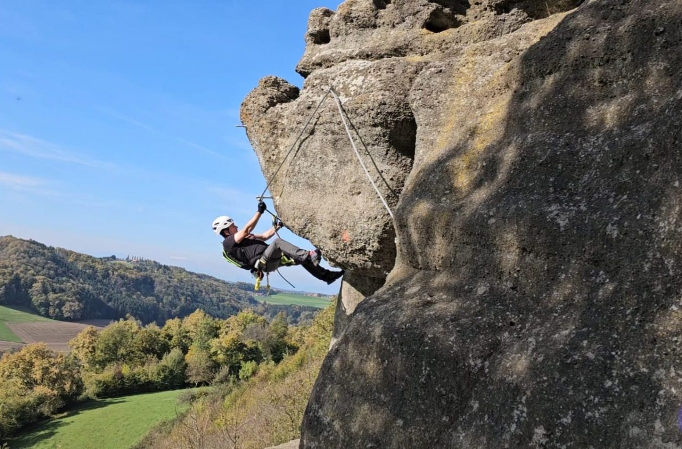Charlotte Klettersteig Manfred Felskletterer in einer vertikalen Position an einer Felswand mit Landschaft im Hintergrund.